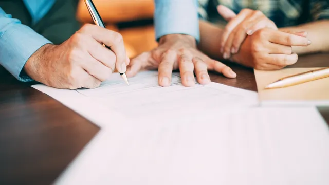 Two people reviewing and signing a business contract at a desk